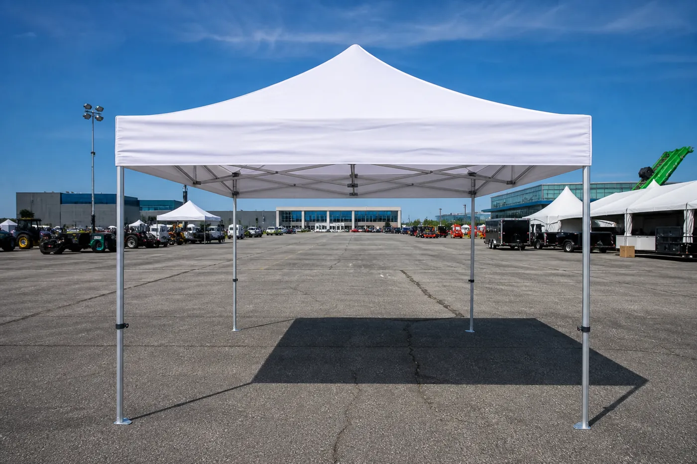White pop-up canopy on an asphalt lot, with a sharp shadow, other small tents and commercial vehicles in the distance.
