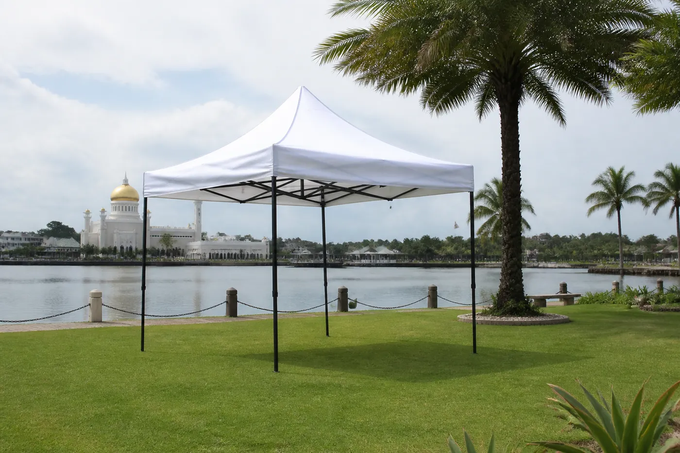 White square pop-up canopy on a waterfront lawn, with a golden-domed building across the water in the distance.