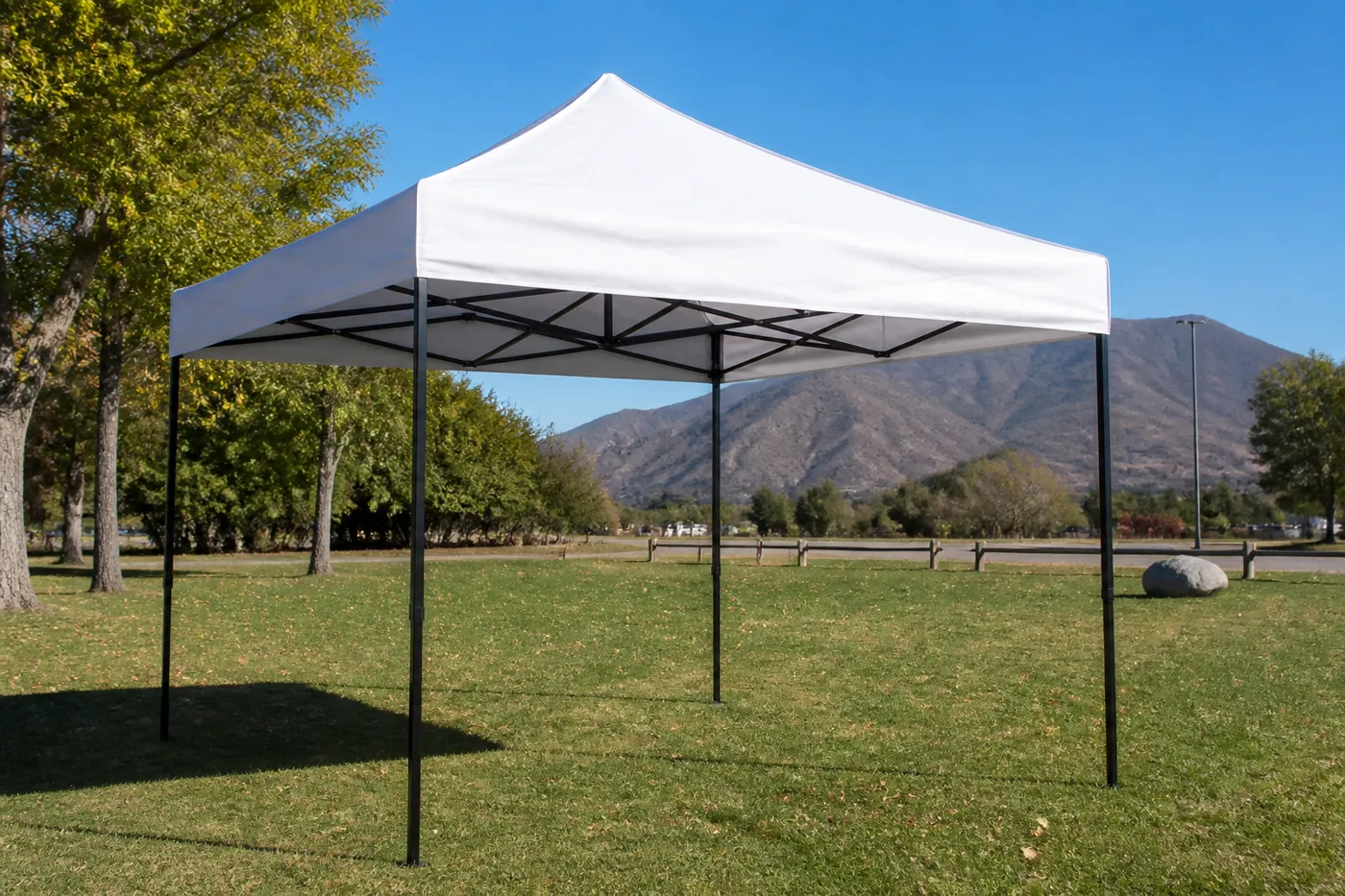 White square pop-up canopy on a grassy field with dry mountains and a wooden fence behind it.
