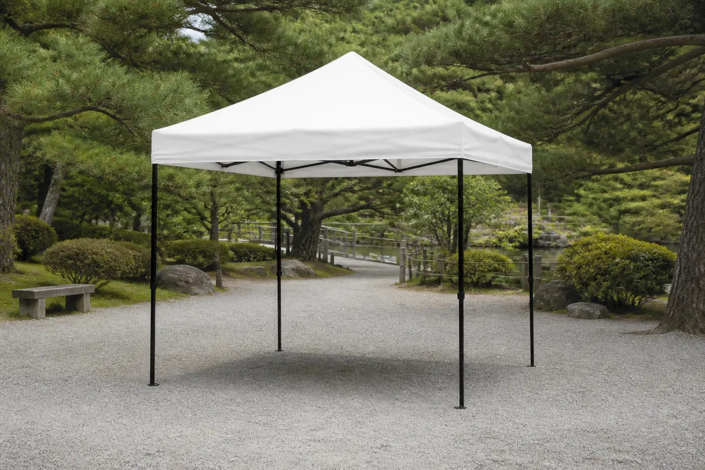 White square pop-up canopy on a raked gravel garden, with pruned pines, a pond and a small wooden bridge beyond.
