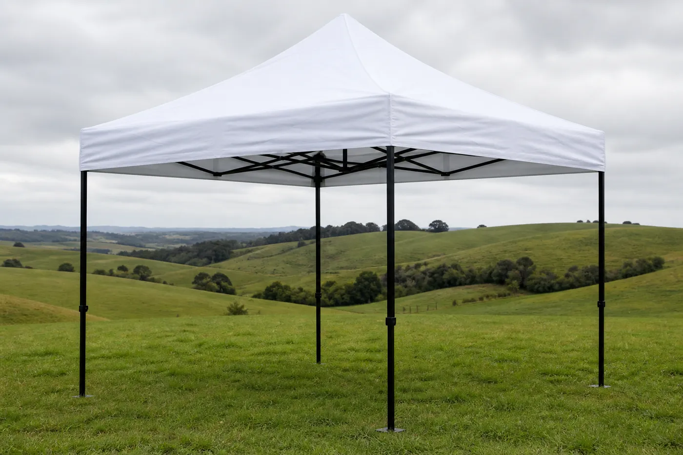 White square pop-up canopy on a grassy pasture with rolling green hills under an overcast sky.